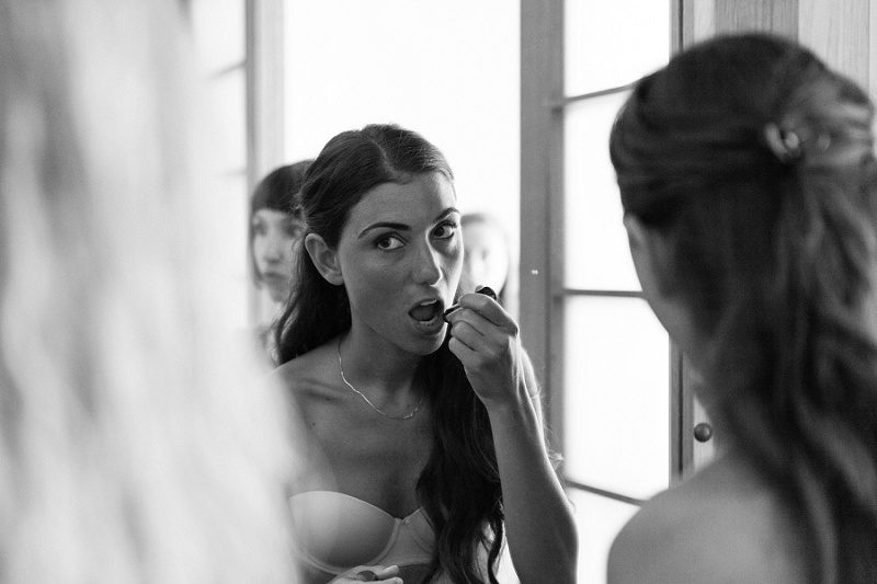 Black and White Image of Bride Putting on Lipstick in Her Suite at Ionian Blue