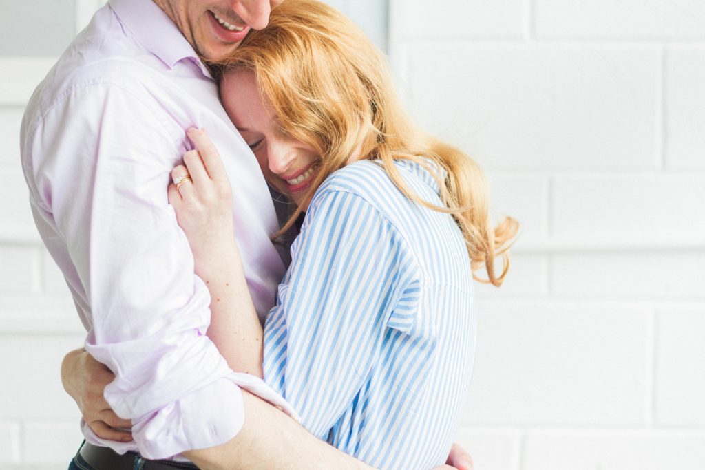 Bride to be cuddles up in her fiance's arms during their engagement shoot