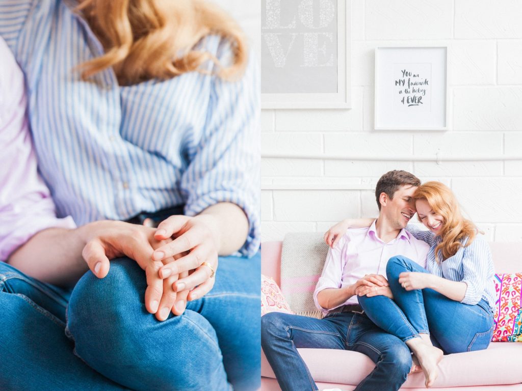 Couple hold hands while sitting on a pastel pink couch