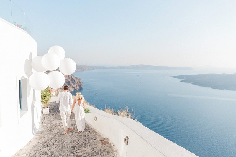 Newlyweds Walking Through Fira with Giant White Balloons