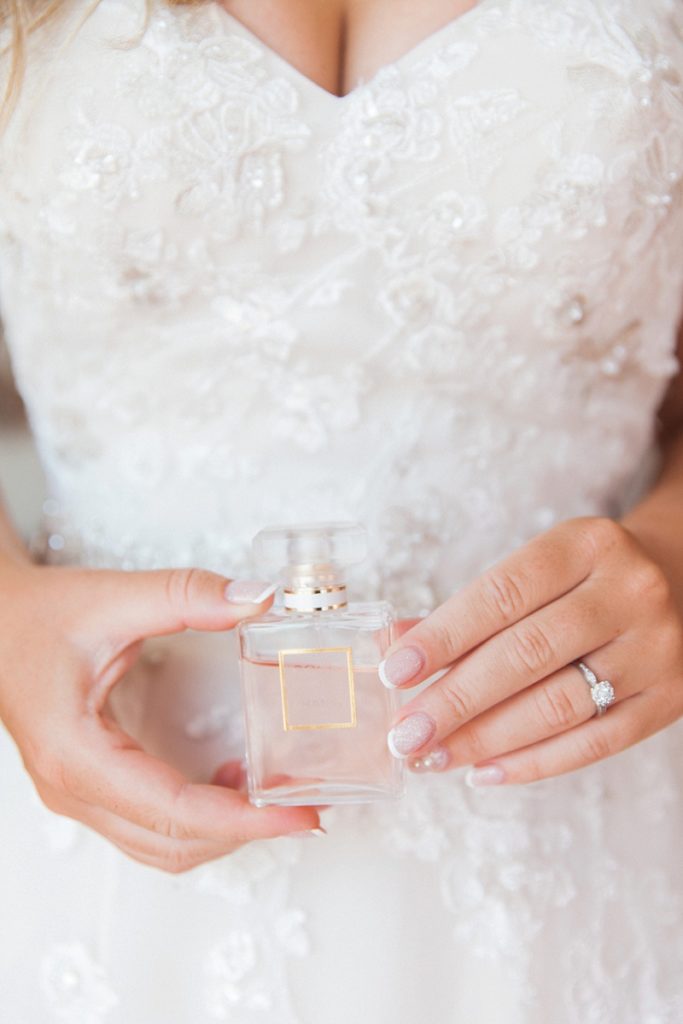Close up image of the bride holding soft pink perfume bottle against her dress