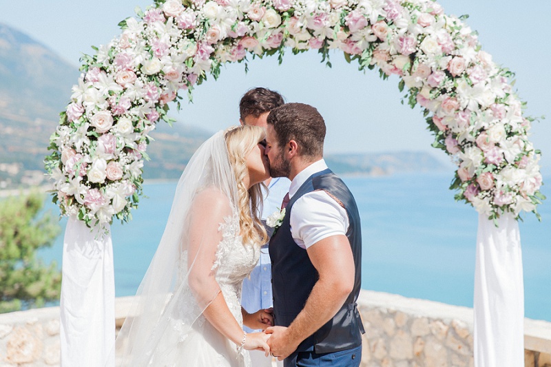 Bride and Groom share their first kiss under a floral arch at their villa wedding on Kefalonia