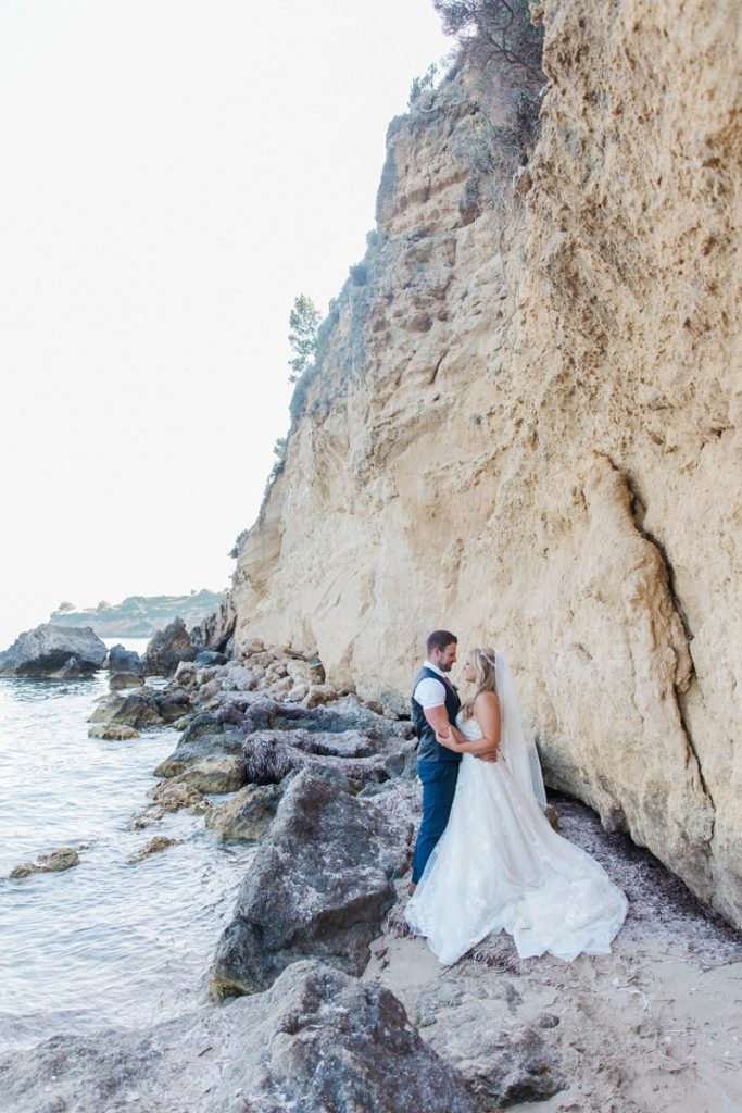 Bride and groom on the beach embracing against a backdrop of dramatic Kefalonian coastline