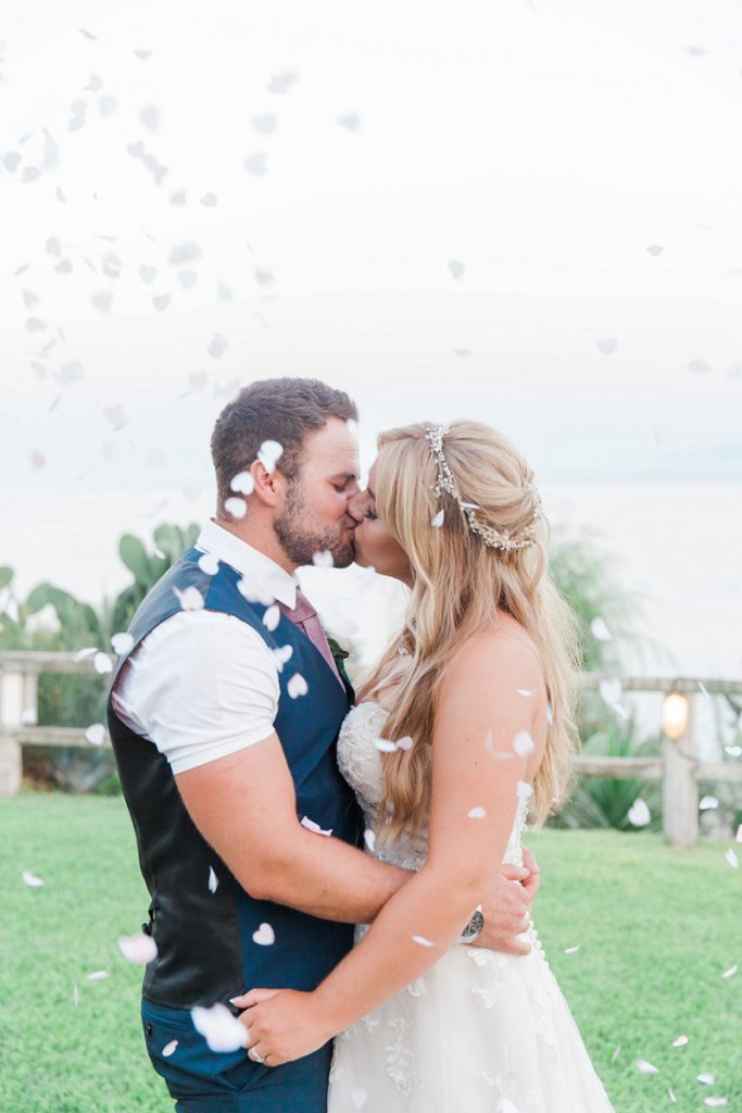 Bride and groom kissing under a shower of confetti at their villa wedding on Kefalonia