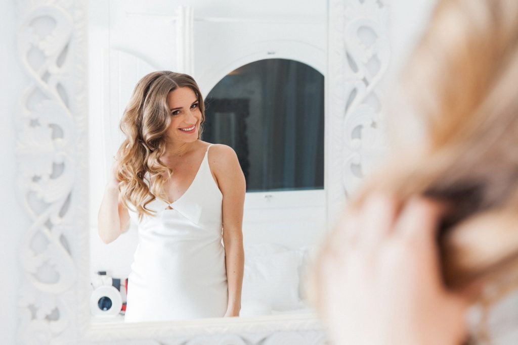 Bride smiles as she does her hair ahead of her elopement at Dana Villas Santorini