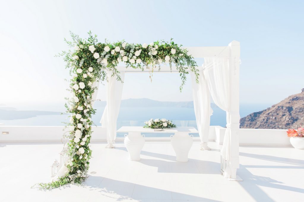White and foliage wedding arch with flowers by Betty Flowers Santorini at Dana Villas Infinity Suites
