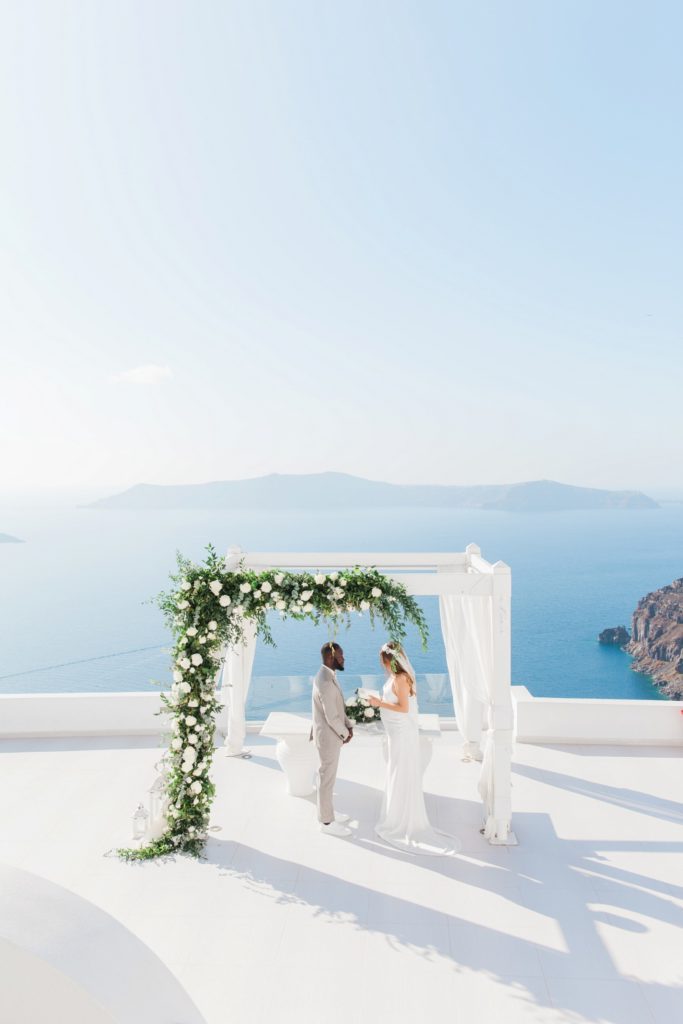 Bride and groom under their wedding arch with a view over the caldera at Dana Villas Santorini