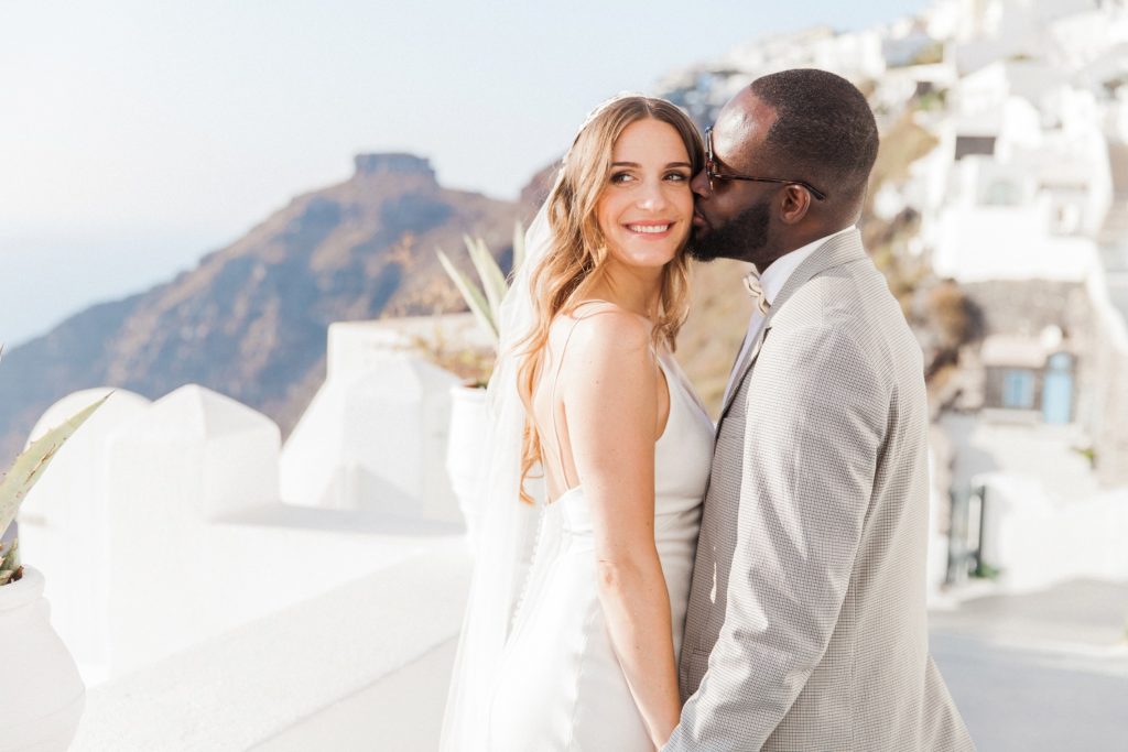 Groom kisses the bride against a view of Skaros Rock in Santorini
