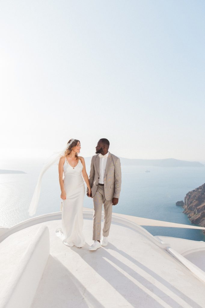 Bride and groom walk across a domed roof at Dana Villas Santorini