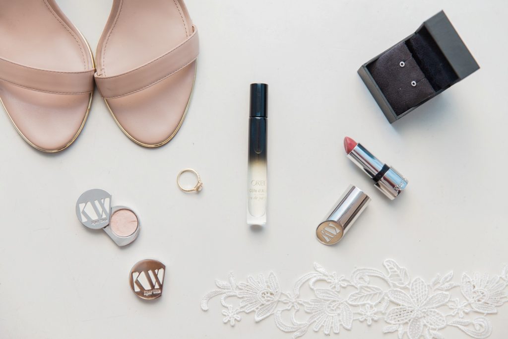 Flatlay of the brides details featuring Carvela heels, Oribe fragrance, jewellery and make-up