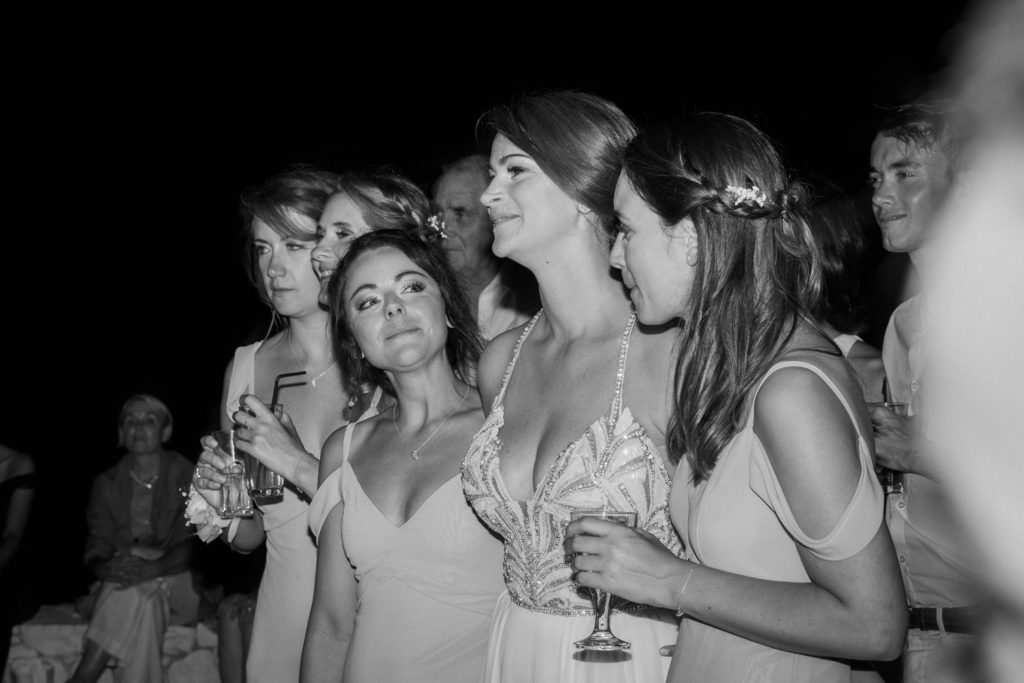 Bride smiles with her friends while her husband serenades her