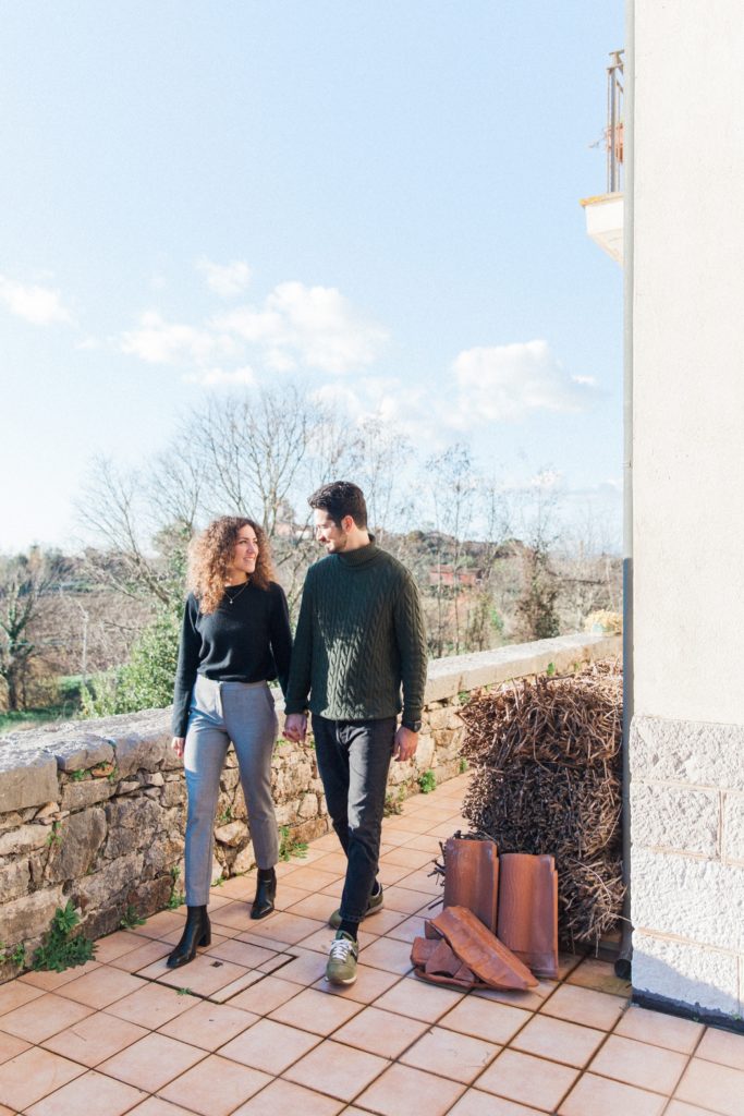 Couple hold hands walking in the garden of an Italian railway house in Semoneta.