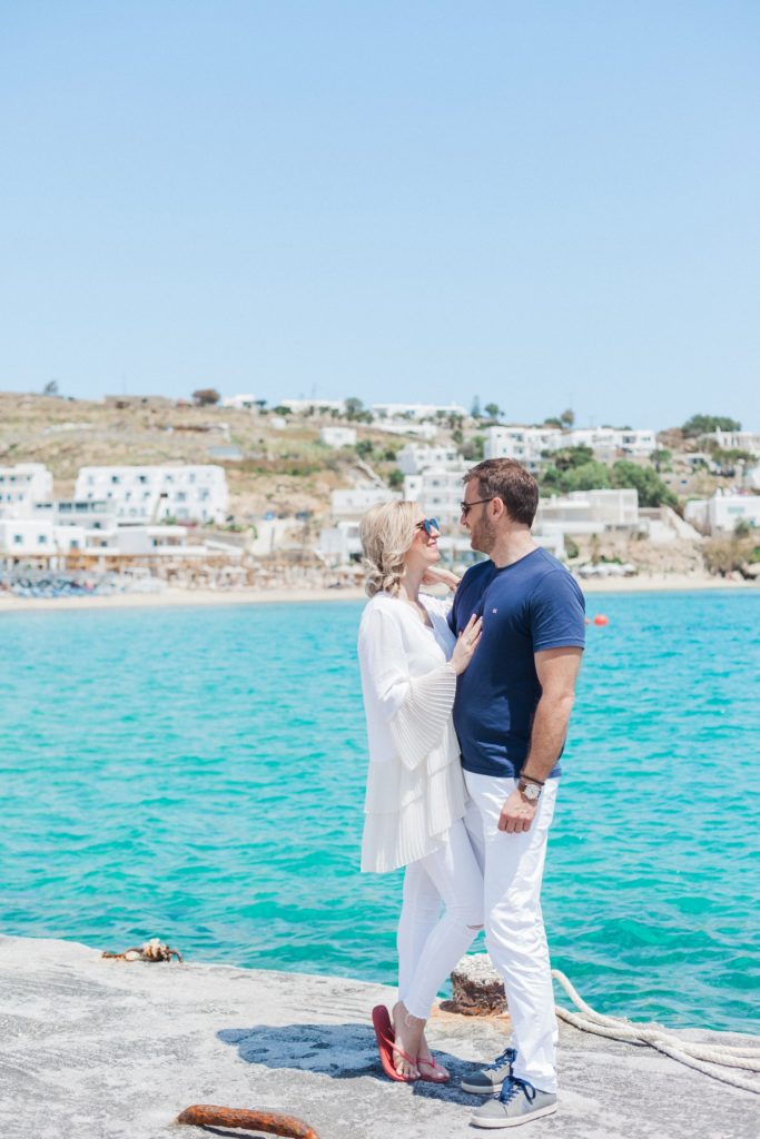 Couple stand near the sea with a view of Platis Yialos beach on Mykonos behind them