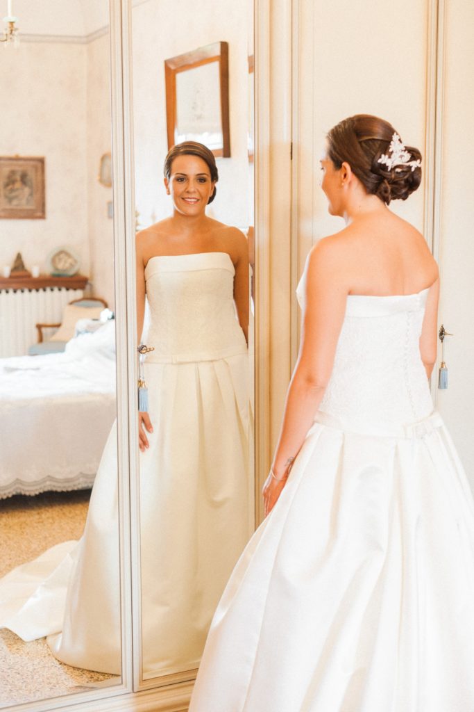 Bride smiles as she looks at herself in the mirror on her wedding morning