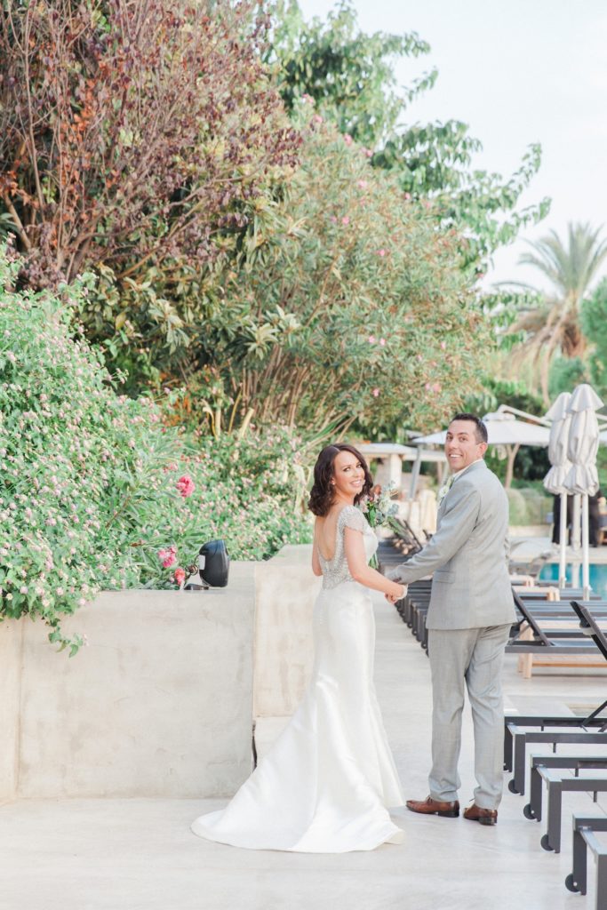 Newly married couple smile as they walk alongside the pool at Domotel Agios Nikolaos in Sivota
