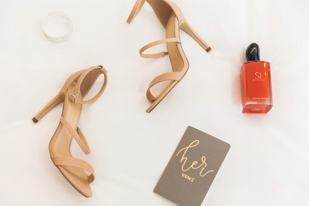 Flat lay of brides details including Carvella heels, vow book, diamond bracelet and Armani fragrance