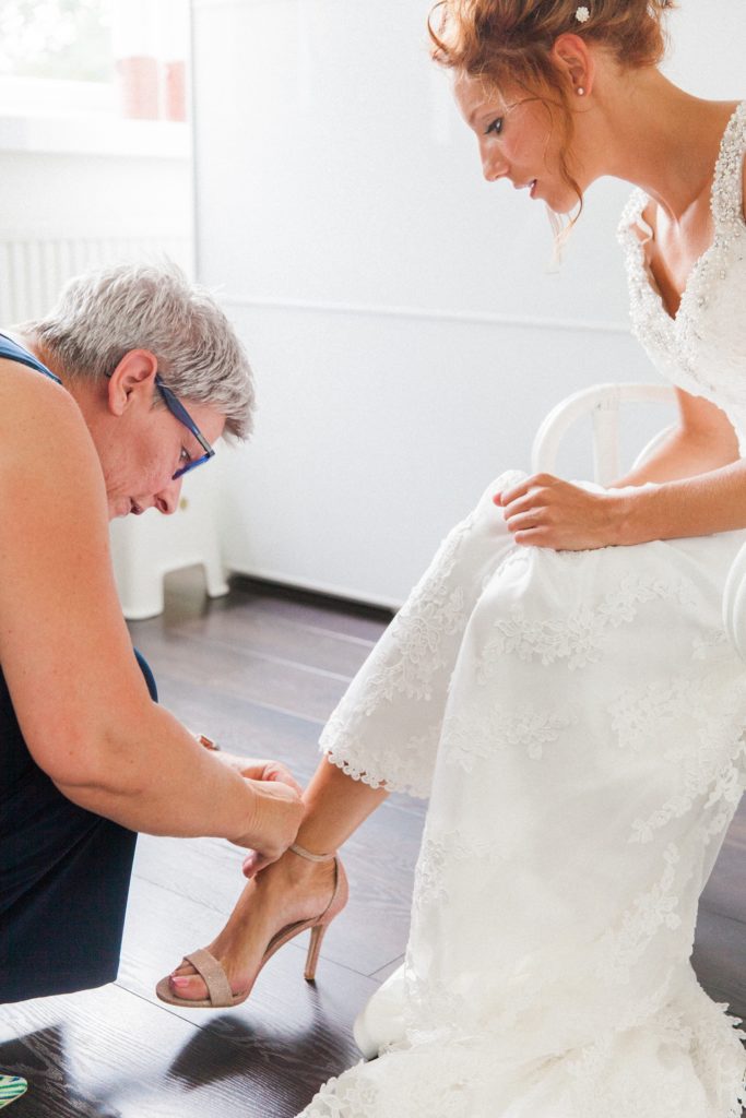 Mother of the bride helps her daughter put on her pink wedding heels from Dune London