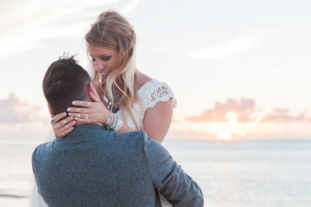 Groom lifts bride up during a romantic moment on the beach at sunset in Mauritius