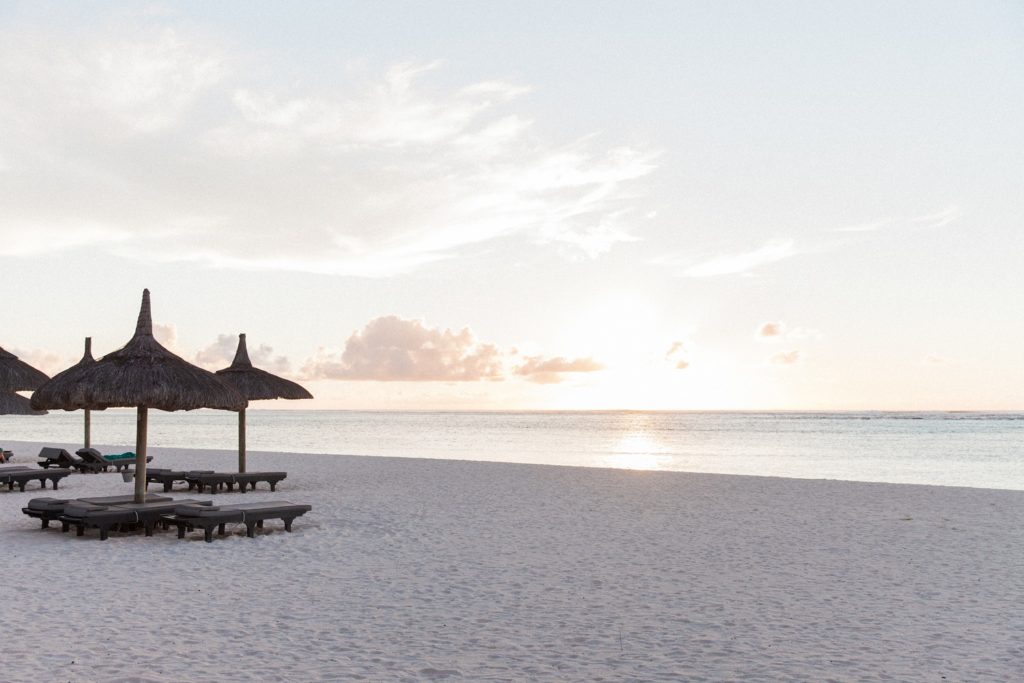 Sunbeds and thatched umbrellas on the beach at sunset in Mauritius
