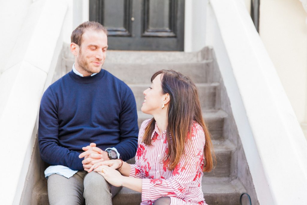 Couple sit holding hands on the front steps of a London town house