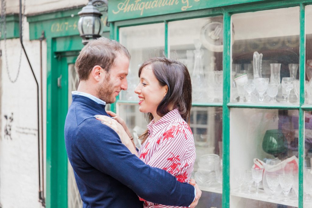 Couple hug in front of an antiques store during their engagement session in Hampstead Village
