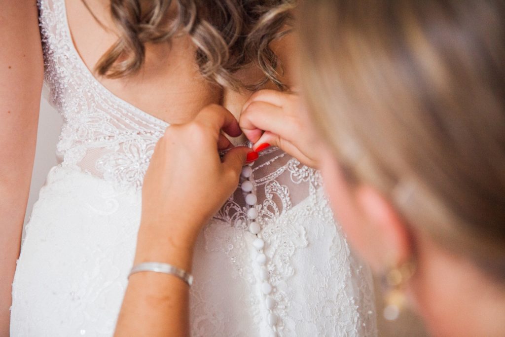 Guest helps bride do up her buttons on the morning of her wedding