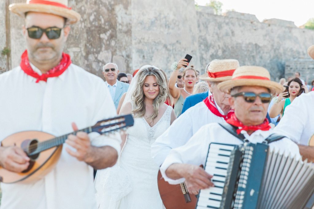Bride smiles as the traditional Greek band leads her and her family to the church in Santa Maura Castle