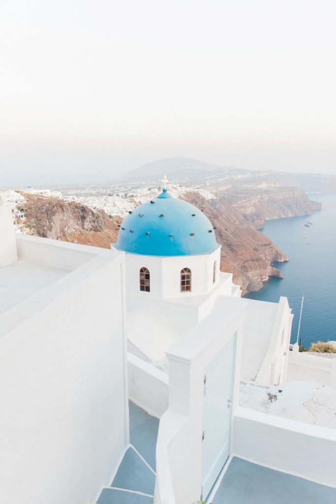 A blue and white Greek church with the cliffs of Santorini in the background