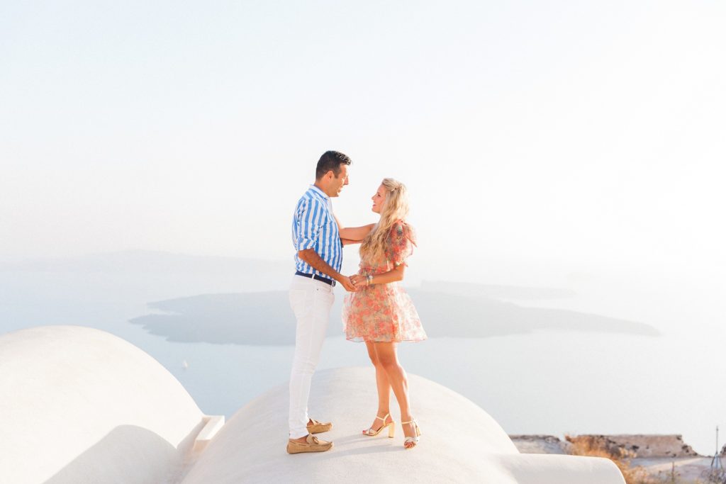 Happy couple stand on a domed roof of a cave house in Santorini