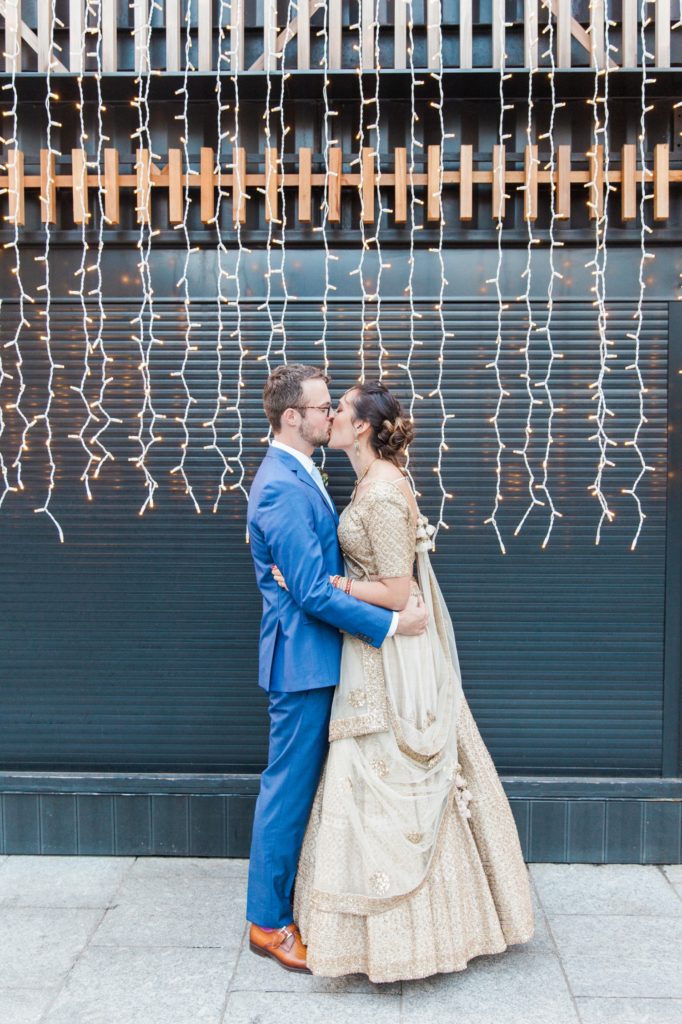 Bride and groom kiss against a backdrop of fairy lights in London