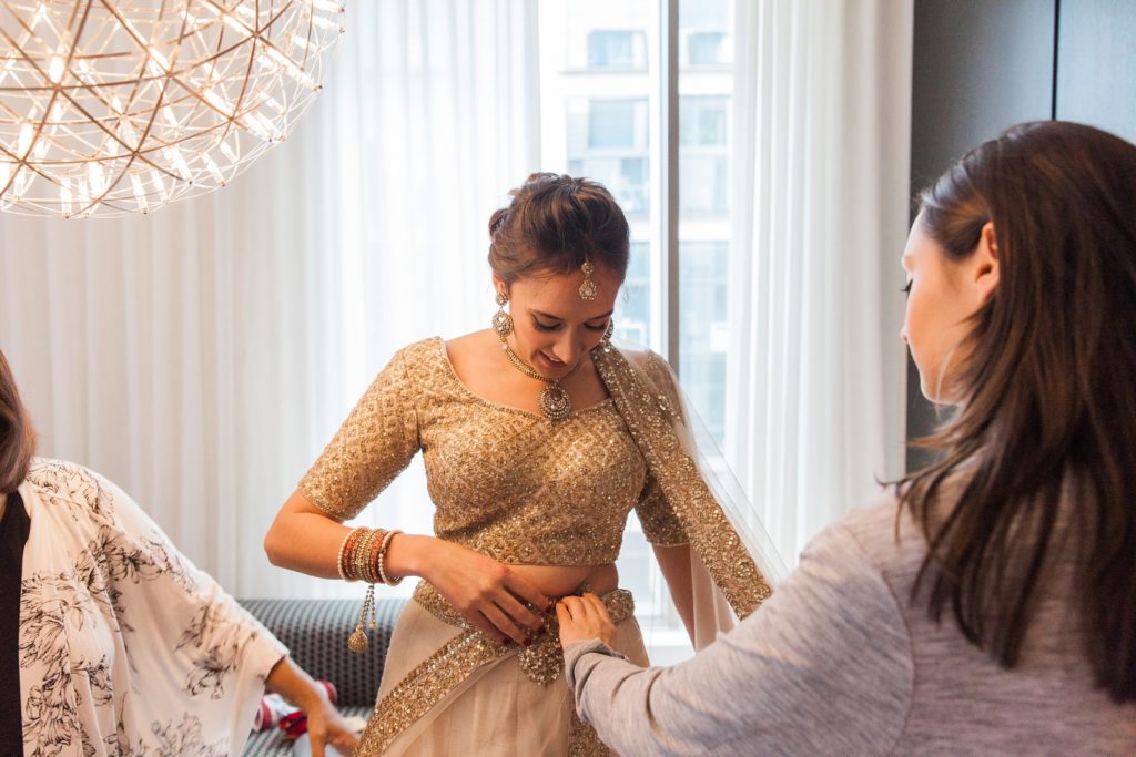 Bride getting helped into her gold lehenga on the morning of her South Place Hotel wedding in London