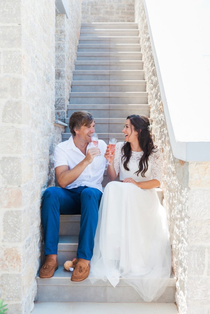 Bride and groom sitting on the steps of their villa toasting with pink prosecco after their elopement