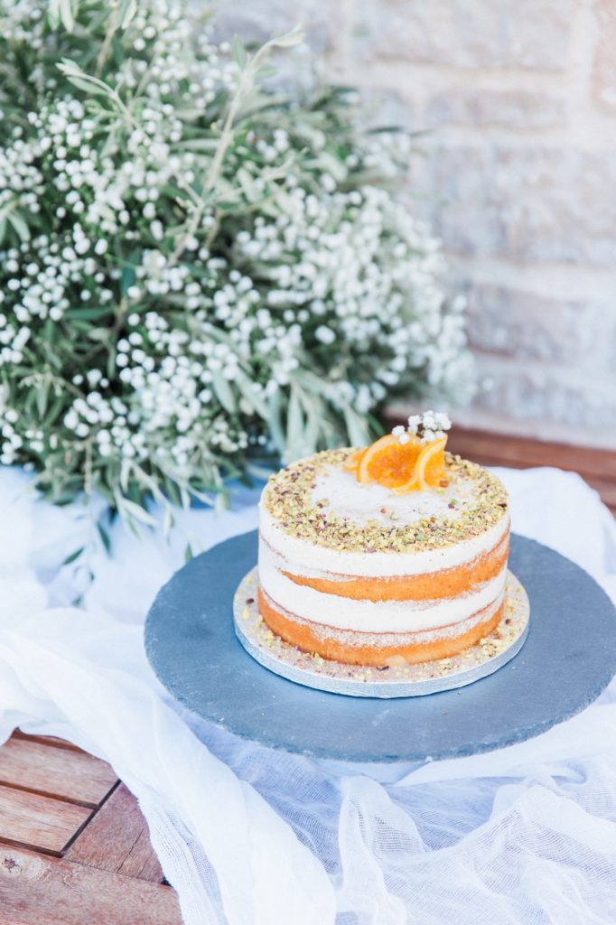 Vanilla and orange naked wedding cake topped with pistacio flakes and orange pieces