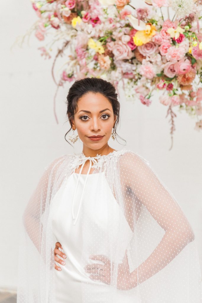 Portrait of a bride wearing a Halfpenny London wedding gown under a spring inspired hanging flower arrangement