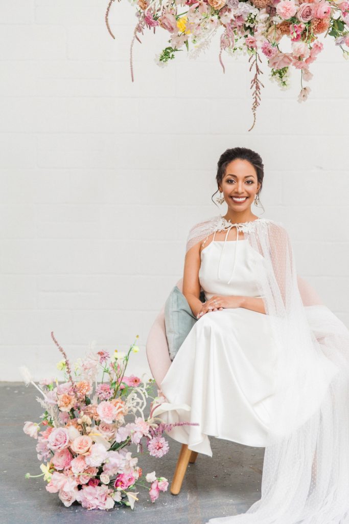 Bride smiles as she sits under a spring inspired hanging flower arrangement