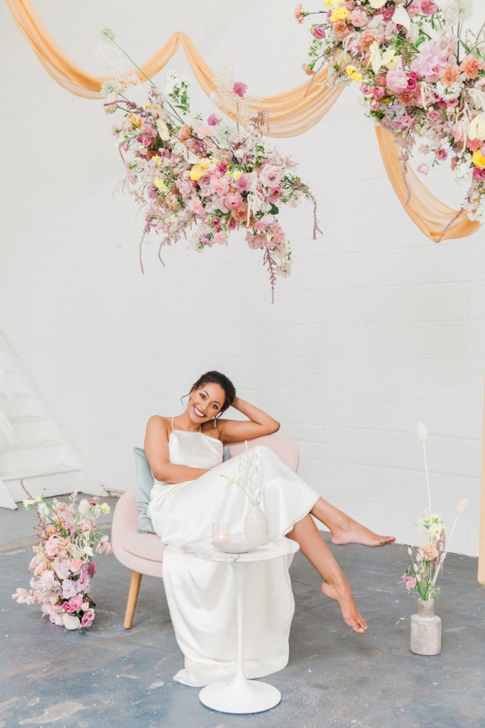 Happy bride sits with her feet up under a hanging spring flower cloud on her wedding day