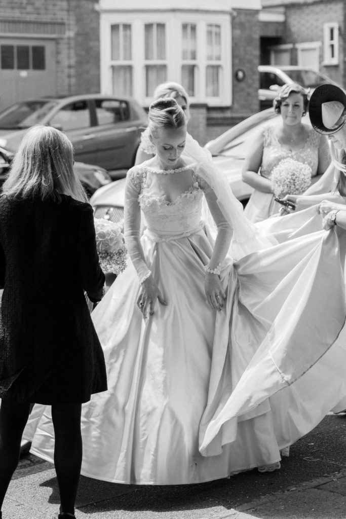 Bride arranges her blush pink wedding gown as she gets out of the car on the morning of her wedding