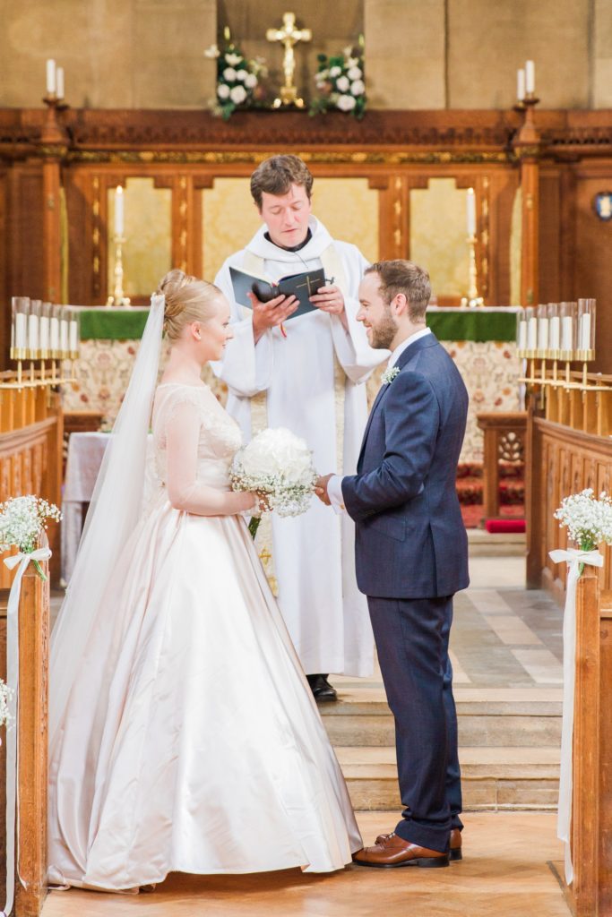 Bride and groom smiles at each other during their wedding ceremony in a traditional English church