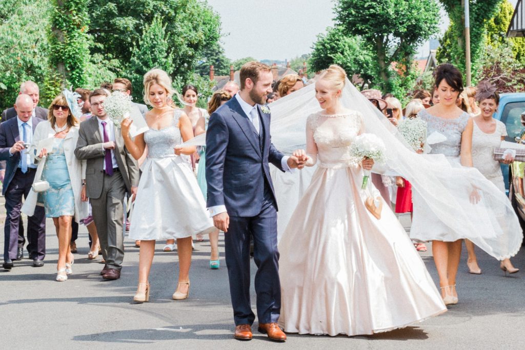 Newly married couple lead their guests from the church through the village to their English garden wedding reception