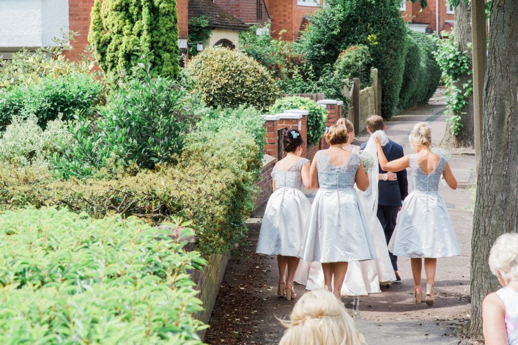 Bride and groom are followed through the streets of the village to their English garden wedding reception