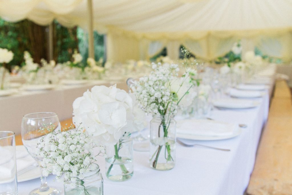 White flowers in small vases down the centre of the wedding tables in a private garden in Leicestershire