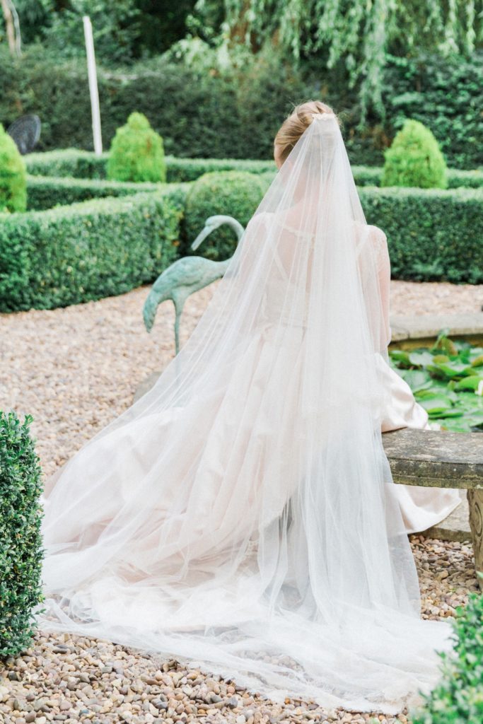 Bride sits next to the pond during her English garden wedding