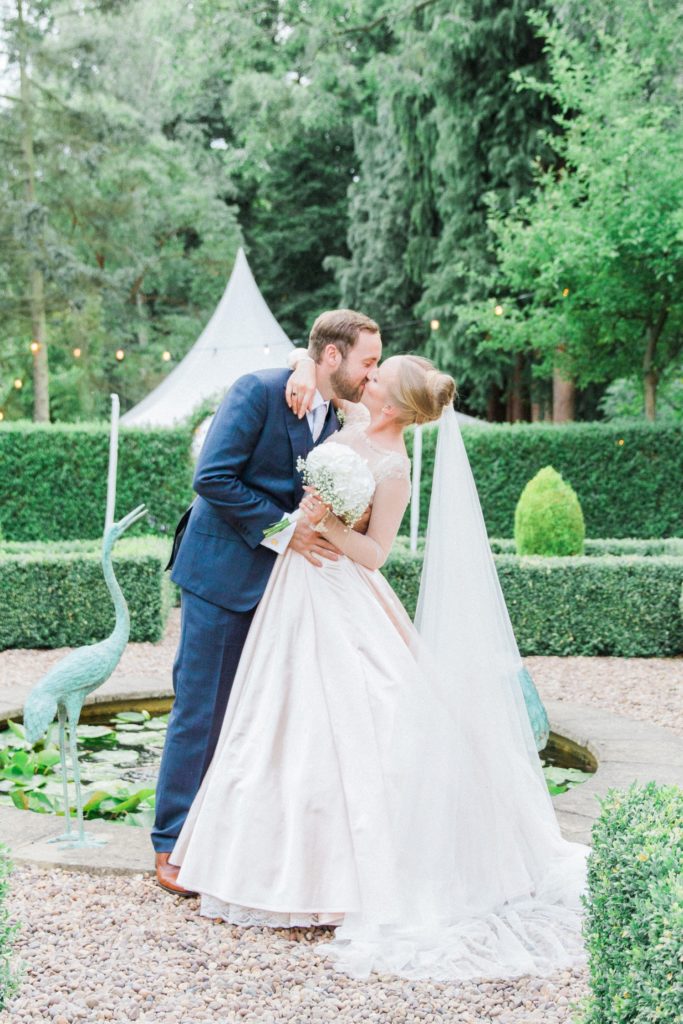 Couple kiss next to a fountain during their English garden wedding
