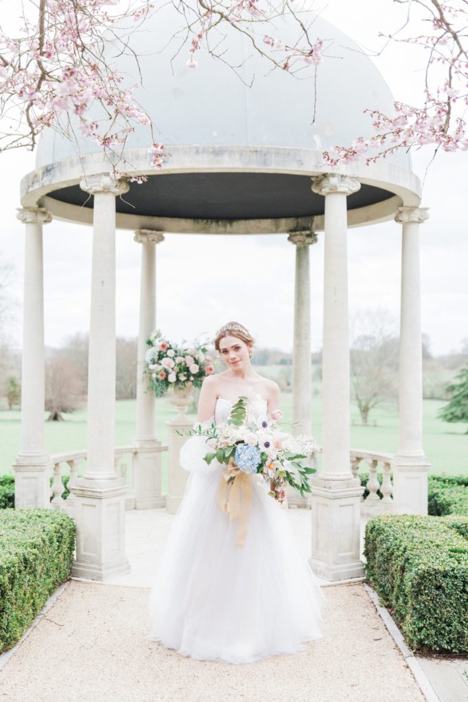 Bride holds a pastel bouquet in front of the wedding gazebo at Froyle Park
