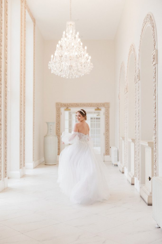 Bride runs down the marble corridor at Froyle Park wearing a Chic Nostalgia wedding gown