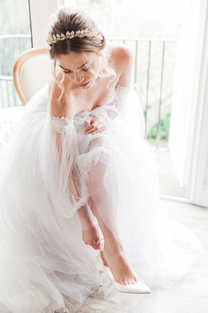 Bride puts on her Harriet Wilde shoes while wearing a Chic Nostalgia wedding dress from Hannah Elizabeth Bridal