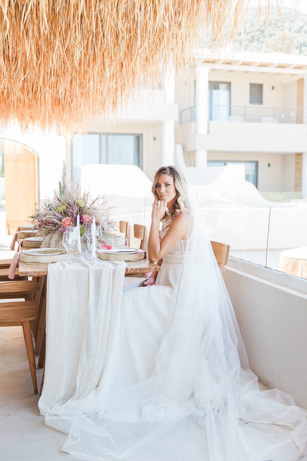 Bride wearing an Atelier Zolotas gown seated at her boho wedding table at Crystal Waters Lefkada in Greece