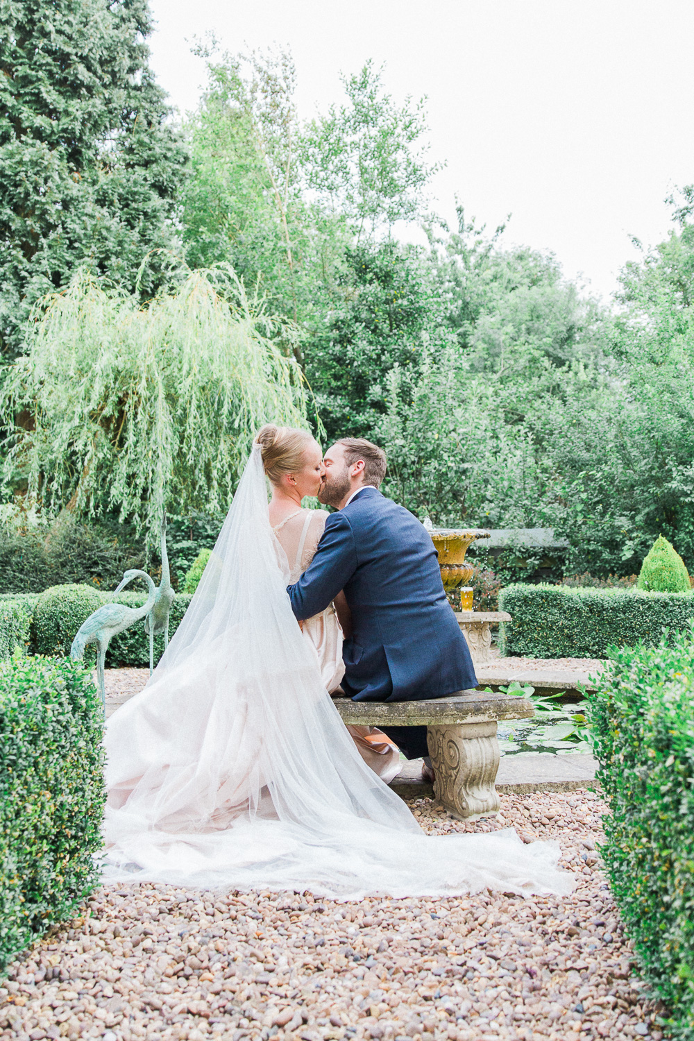 Bride and groom kissing on a bench at their English garden wedding