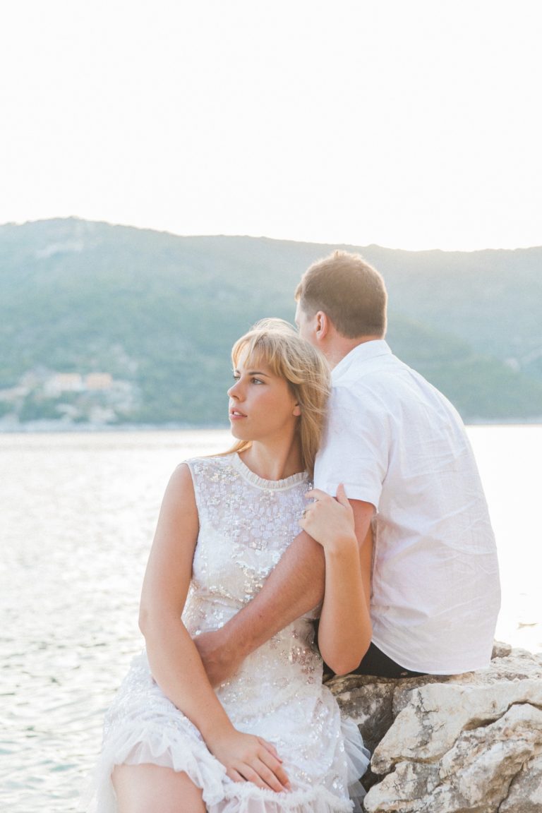 Couple sitting on the rocks over looking the sea during their sunset honeymoon photography session in Lefkada