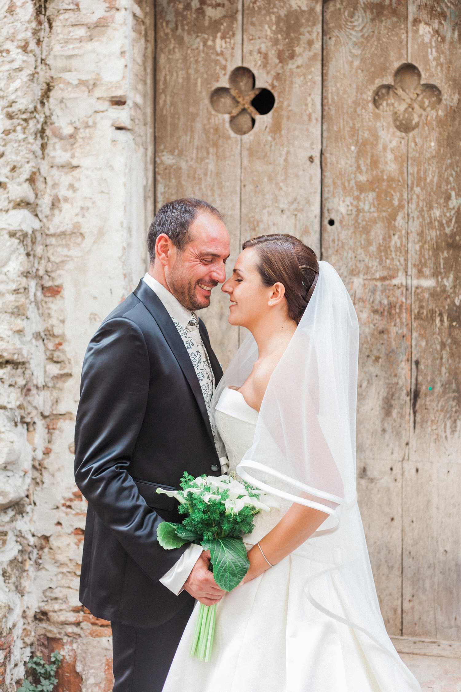 Italian bride and groom stand together in front of a beautiful old door during their wedding at the Convivium Hotel in Vasto Abruzzo